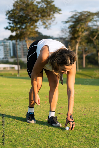 A latin hispanic female golfer bends to place a golf ball on the green course