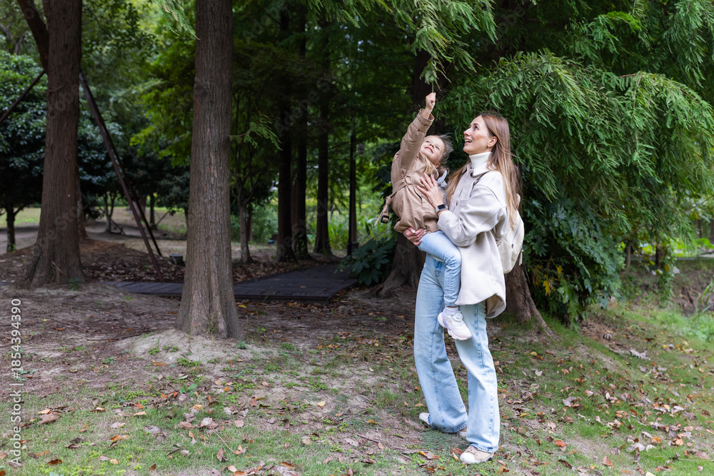 Fototapeta premium Young woman holding child while pointing at tree in a park