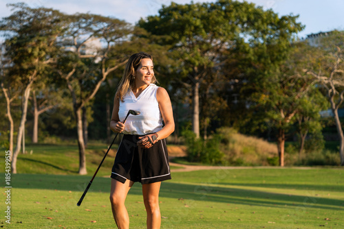 Smiling latin hispanic woman holding a golf club on a green course, enjoying an outdoor sport and leisure activity