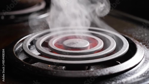 Water droplets sizzle and steam emanates from a glowing red electric stovetop coil