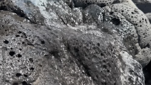 Water cascading over porous volcanic rocks creating a natural textured surface abstract background