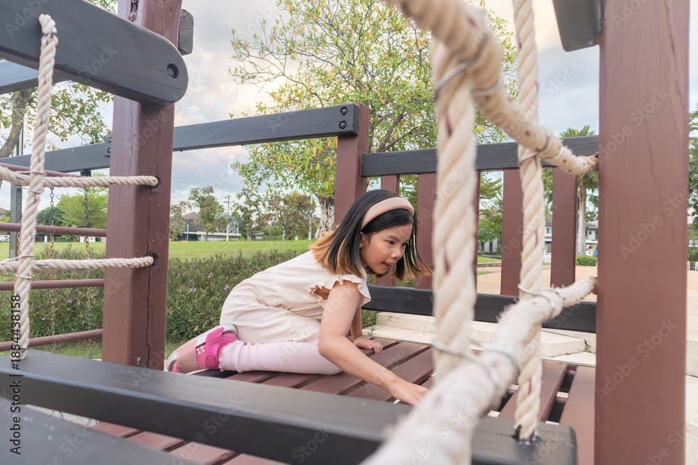 Obraz premium Excited Asian girl laughing happily on the high platform of a wooden playground structure