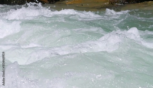 Close-up of churning water, showcasing white foam and translucent droplets. The liquid flows rapidly, creating textures, movement, and dynamic energy