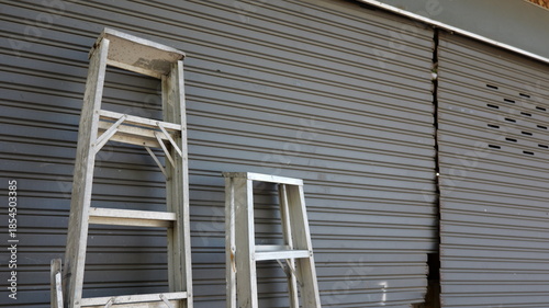 Wooden Ladders Leaning Against Gray Shuttered Storefront with Visible Crack