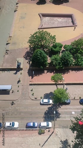 City street on sunny summer day. Parked cars, tram tracks, green trees, non-working fountains, walking people and cyclists riding on asphalt road near square in city. City landscape. Top view Vertical
