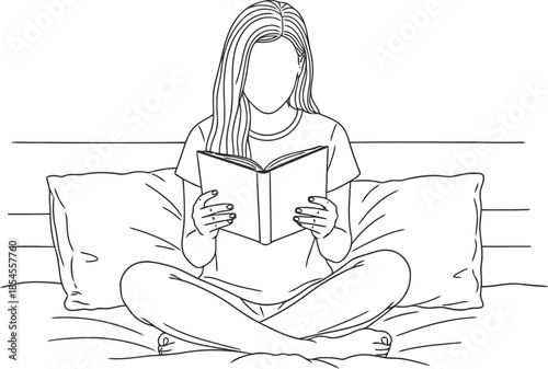 Young woman sitting cross legged on bed reading a book