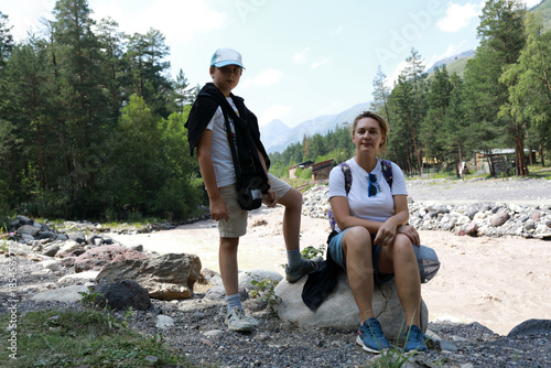 Woman and boy rest near mountain river during excursion to narzan meadow from Terskol