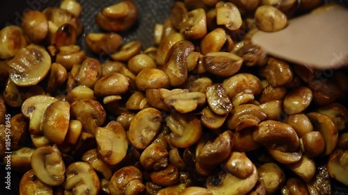 Close-up slow motion of small golden button mushrooms being fried in a pan on a home gas stove in the kitchen.