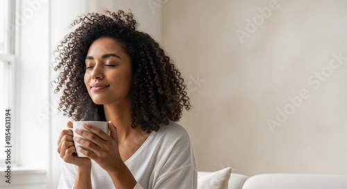 Serene young woman with curly hair enjoying a mindful moment with a warm drink at home.