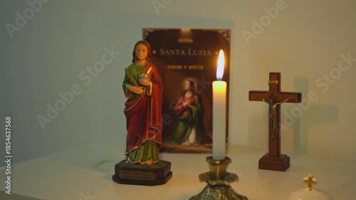 Religious setup with a statue of Saint Lucy a devotional booklet wooden crucifix and a burning candle on a table with warm light creating a sacred atmosphere for Christian prayer