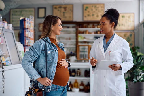 Happy pregnant woman consulting with pharmacist in drugstore.