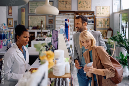 Happy couple consulting with black pharmacist while buying vitamins in drugstore.