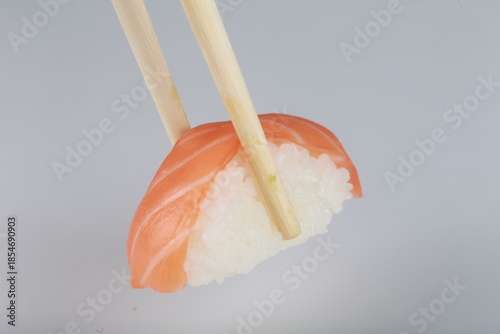 Nigiri au saumon tenu par des baguettes sur fond blanc