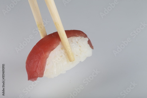 Nigiri au thon rouge tenu par des baguettes sur fond blanc