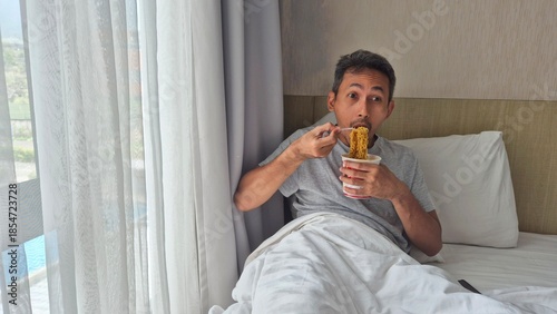 Asian man eating noodles at bedroom