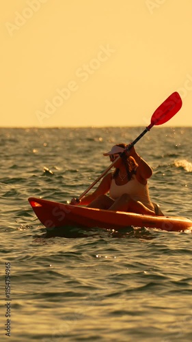 Kayaking woman paddles aggressively at sunset on the ocean water during golden hour sports activity Vertical video.