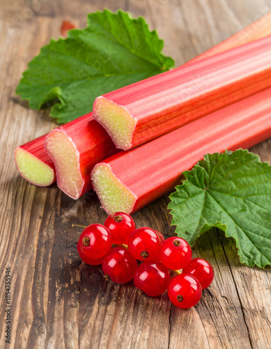 Raw Rhubarb Stems and Red Currant Berries with Foliage on Rustic Wood
