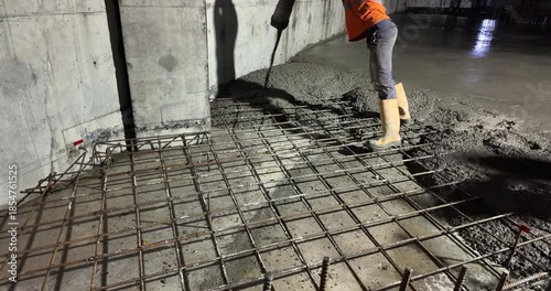close up of a construction worker pouring concrete onto a rebar grid at night.