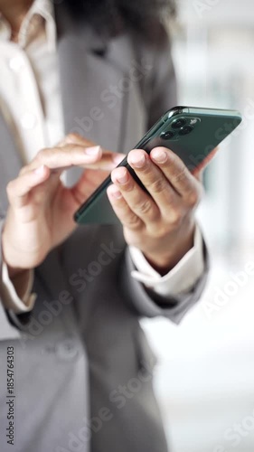 Close up of African American female hands holding using mobile phone in business office. Businesswoman in a suit working on app, typing message, chatting online, browsing smartphone. Vertical video