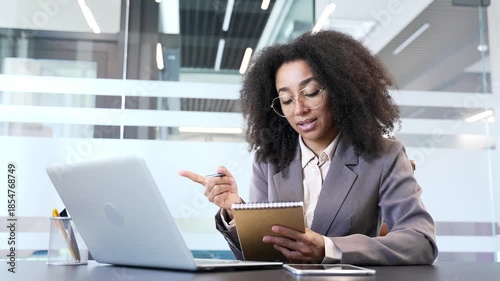 African american businesswoman watching video call online conference taking notes looking at laptop screen in office. Female worker listening remote business training, talking communicates with tutor