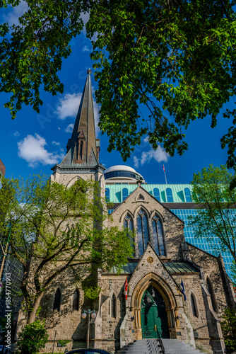 Stone church with tall steeple framed by trees against blue sky