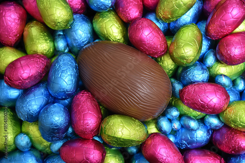 Pile or group of multi colored and different sizes of colourful foil wrapped chocolate easter eggs in blue, pink, red, yellow and lime green with a large brown milk chocolate egg in the middle.