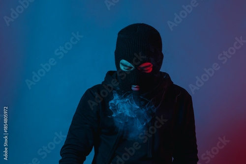man in hoodie and balaclava looking down and blow smoke out