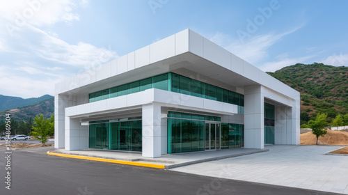 A modern white commercial building with glass and doors stands against a backdrop of rolling hills and a partly cloudy sky on a bright sunny day.