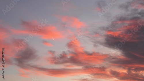 A plane flies through a colorful sky filled with pink and gray clouds during sunset. The scene captures the beauty of aviation and nature.