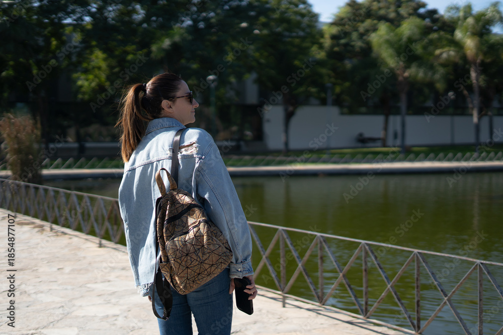 Obraz premium Woman with backpack walking by a pond enjoying sunlight