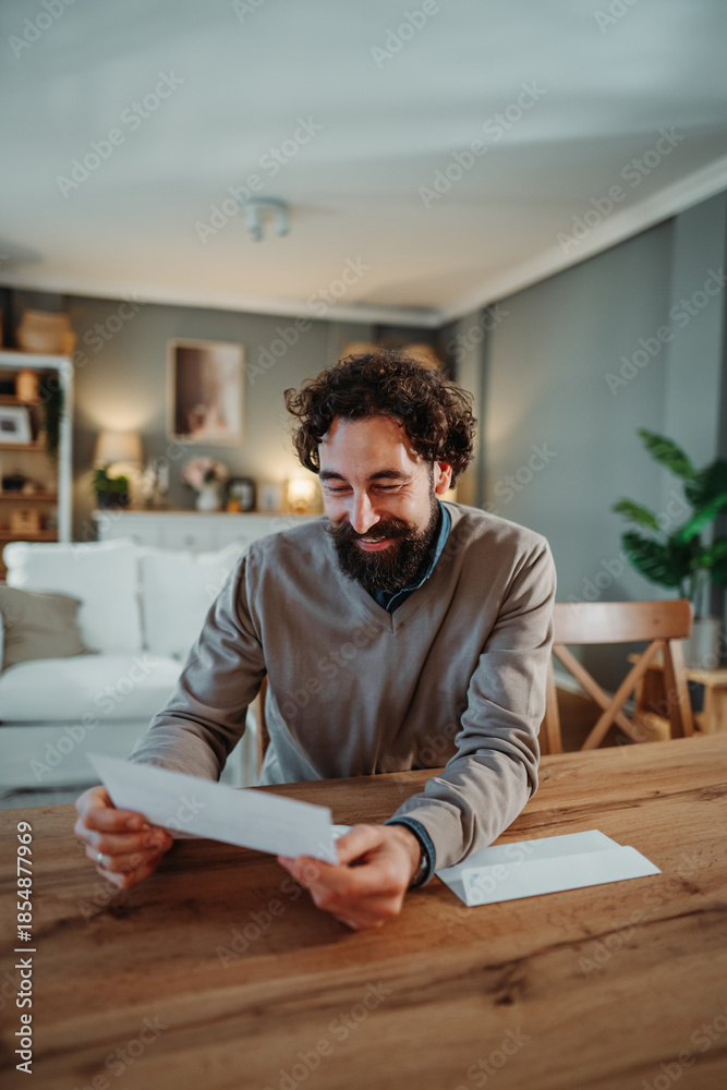 Obraz premium Man reading letter smiling receiving good news at home