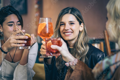 Bild auf Leinwand Three young women toasting with cocktails in a bar, friendship and social lifest
