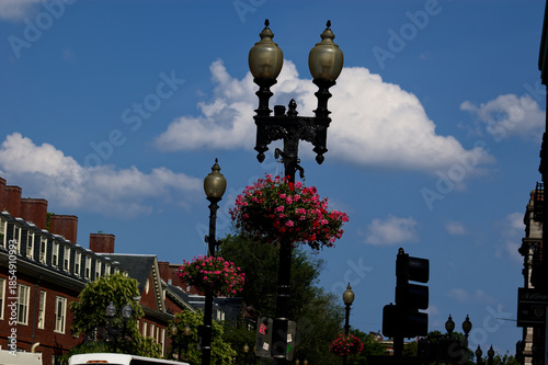 Charming Urban Street: Vintage Black Lamps With Flower Baskets, Historic Buildings Under Blue Sky