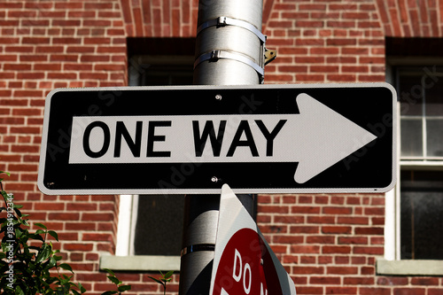Urban Navigation: One Way Street Sign Mounted on Metal Pole Before Red Brick Building, Indicating Direction