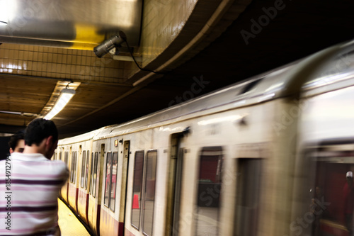 Urban Commute: Man In Striped Shirt Briskly Passing Subway Train on Dim Platform During Rush Hour
