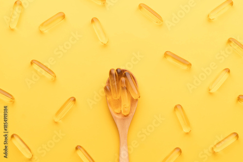 Oil softgel capsules in wooden spoon on yellow background. Nutritional supplement contains fish oil, omega 3, omega 6, omega 9, vitamin e, vitamin d and vitamin a.