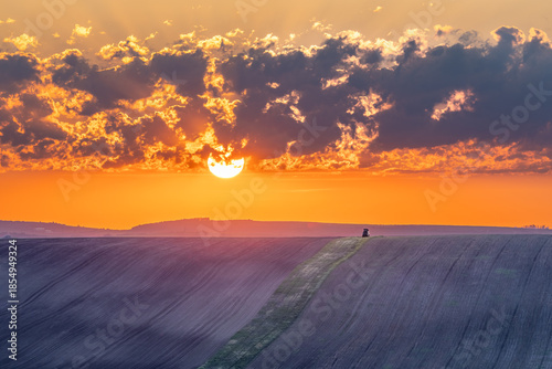 A vibrant sunset over a vast, tilled field with a vehicle on the horizon.