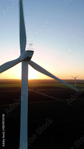 Aerial drone view of large wind turbine power plant, windmills producing renewable energy electricity, flat farm landscape at sunset, beautiful colours, United Kingdom. 