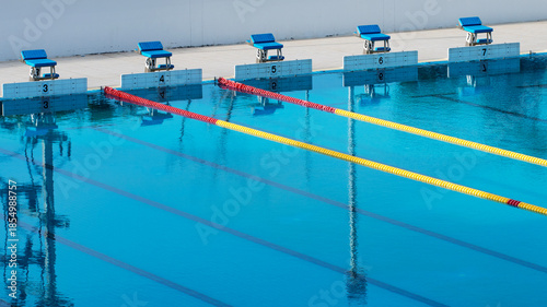 Swimming pool lanes for competition sport, perspective view of starting blocks and reflections on water.