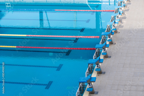 Swimming pool lanes for competition sport, perspective view of starting blocks and reflections on water.