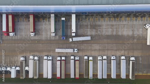Top down aerial view of heavy semi trucks and trailers parked in loading bays at large distribution centre. Transport and logistics hub for import export in Milton Keynes, United Kingdom. 