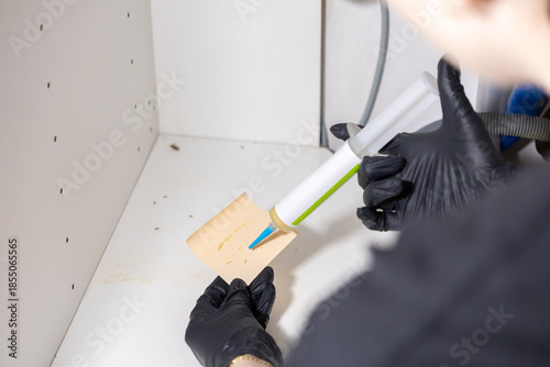 Schilderij op canvas Gloved professional hand applying cockroach pest control gel bait inside a dirty