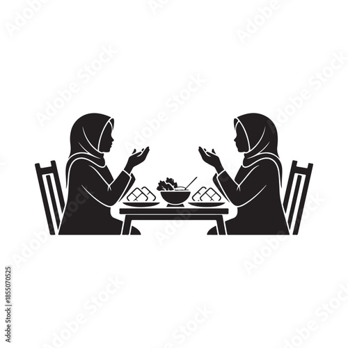 Two women in hijabs share a meal together at a small table