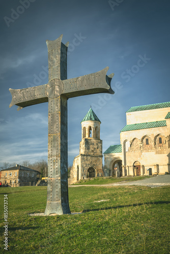 Wallpaper Mural Large metal cross in front of historic stone church and bell tower under dramatic sky, photographed on a sunny day in Kutaisi, Georgia. Religious architecture with spiritual and peaceful atmosphere Torontodigital.ca