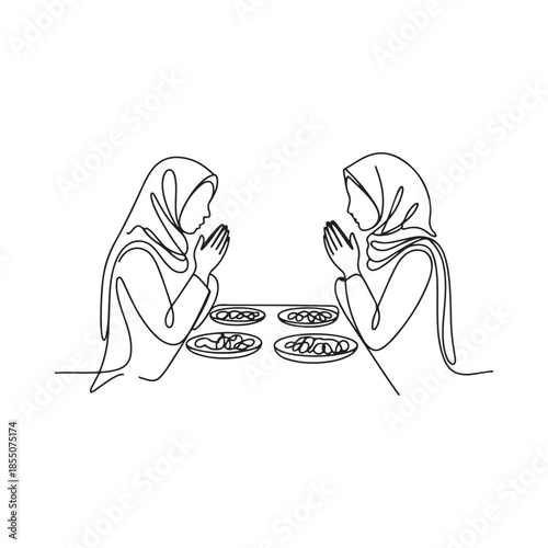 Two women with hijabs praying with food in front of them