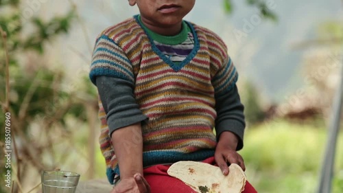 A rural Indian boy eats simple food with bread and tea while sitting outdoors in an Uttarakhand village. The scene reflects poverty, daily nutrition, childhood, and village lifestyle.