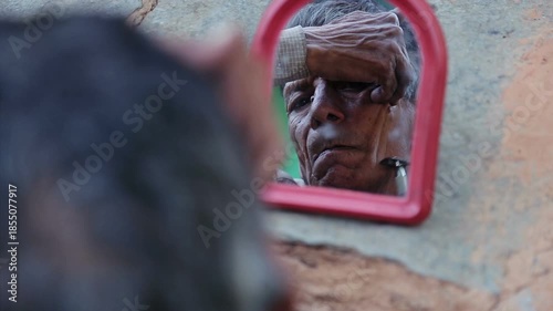 An elderly Indian man shaves his beard using a small mirror outdoors in an Uttarakhand village. The scene reflects poverty, daily routine, self care, and rural mountain lifestyle.