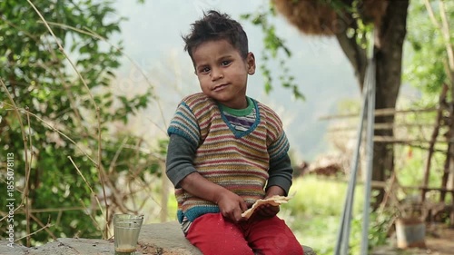 A rural Indian boy eats simple food with bread and tea while sitting outdoors in an Uttarakhand village. The scene reflects poverty, daily nutrition, childhood, and village lifestyle.