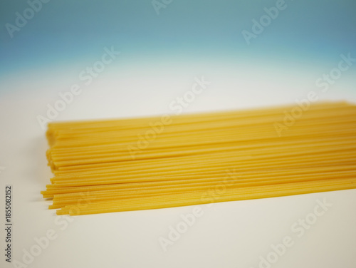 Wallpaper Mural Uncooked spaghetti pasta spread in a flat layer on white surface with blue gradient background, minimal food image of dry Italian noodles and cooking ingredients Torontodigital.ca