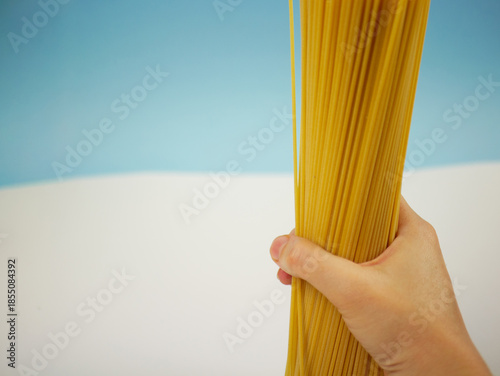Wallpaper Mural Vertical view of a large bundle of uncooked spaghetti pasta held by a hand on blue and white background, modern food photo of dry Italian ingredients Torontodigital.ca